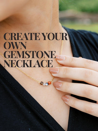 Women daintily touching a gemstone necklace with four gemstone beads on it.