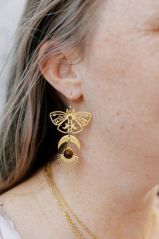 May include: Gold tone earrings with a crescent moon, sunburst, and butterfly design. The sunburst features a brown tiger's eye gemstone.
